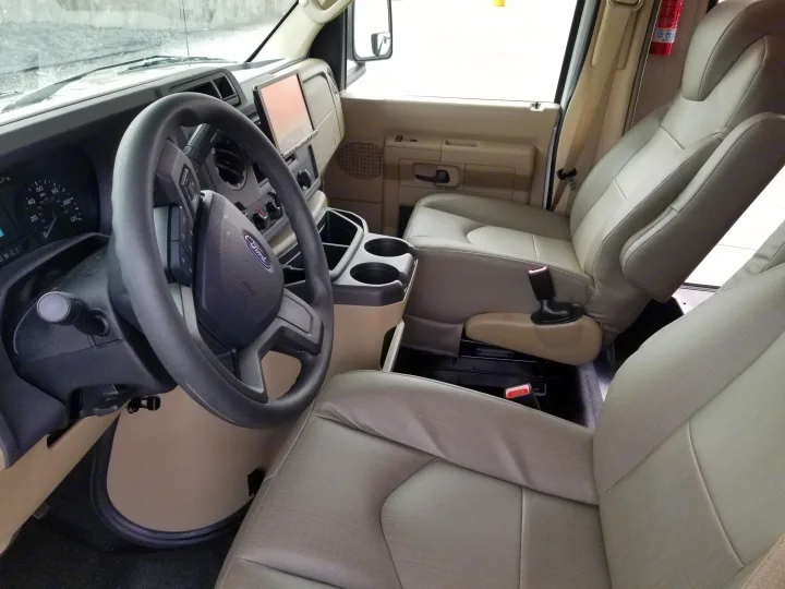 Spacious RV rental cabin: driver's area with Ford steering wheel, dash, infotainment screen, cup holders, and passenger seat.. Entegra Coach Other 2021