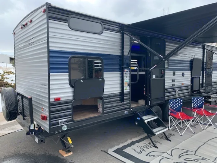 Spacious Grey Wolf rv rental travel trailer, fully set up with extended awning, entry steps, and outdoor chairs on a mat.. Cherokee Grey Wolf 27DBH 2021