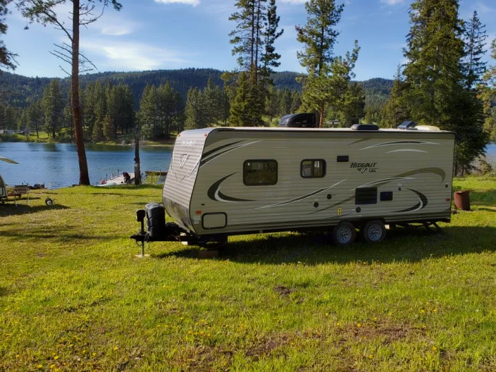 This RV rental, a travel trailer, is parked by a scenic lake with mountains, perfect for an outdoor getaway.. Keystone Hideout 2017