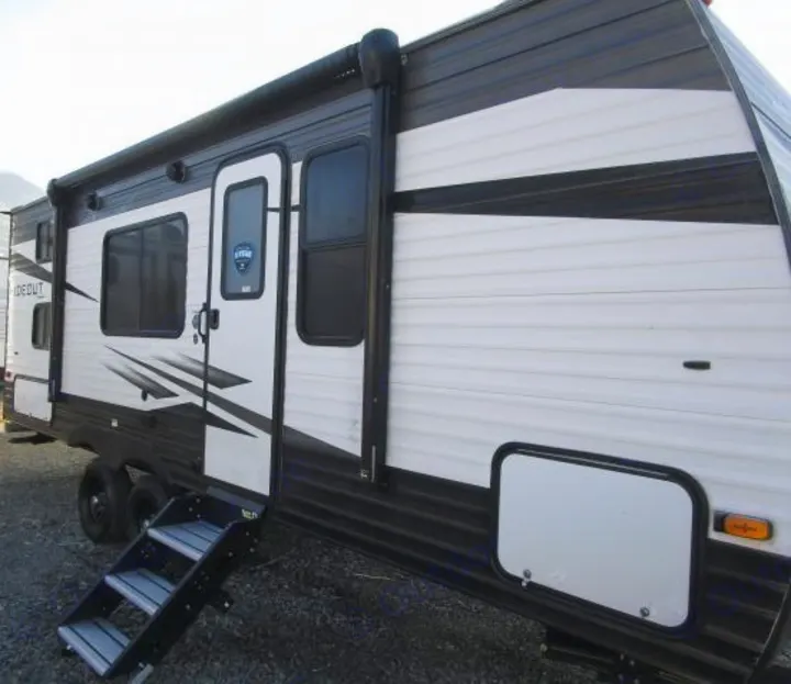 Side view of a modern white and black travel trailer, featuring its entry door, windows, and deployed steps for RV rental.. Keystone Hideout 2021