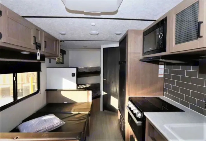 Spacious RV rental interior featuring a kitchen with microwave and stove, convertible dinette, bunk beds, and overhead storage.. Keystone Hideout 2021