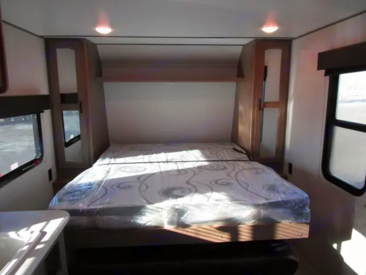 RV rental interior shows a compact sleeping area with a new mattress in plastic, overhead storage, and side windows.. Keystone Hideout 2021