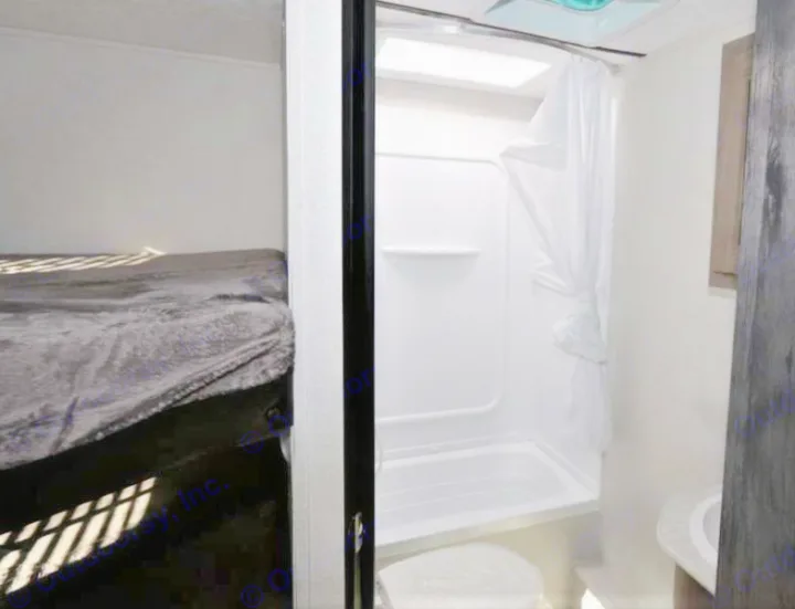 Compact RV rental interior: cozy bedroom with bed and an adjacent bathroom featuring a shower/tub combo and sink.. Keystone Hideout 2021
