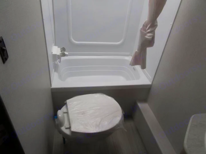 Compact RV rental bathroom: features a white toilet covered in plastic, and a small bathtub/shower with a light curtain.. Keystone Hideout 2021