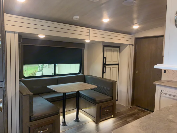 Modern RV rental interior showcasing a spacious U-shaped dinette with table, compact kitchen, and bright lighting.. Keystone Cougar Half-Ton 2021