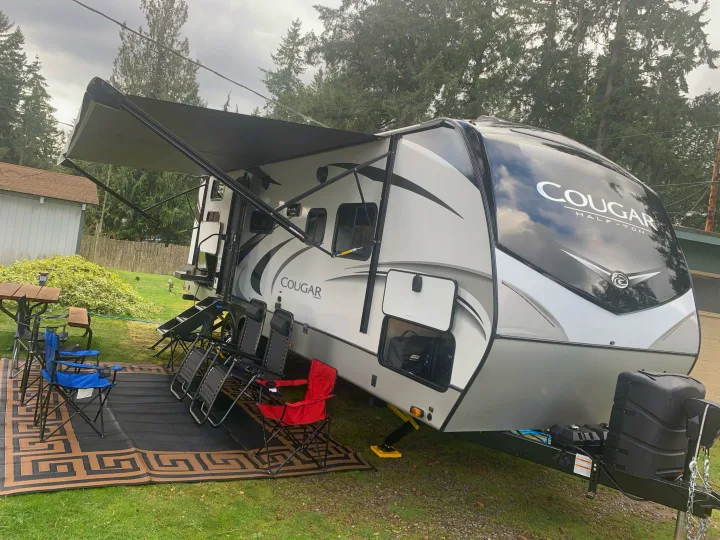 This RV rental is set up for outdoor comfort with an extended awning, camping chairs, and a mat on the grass.. Keystone Cougar Half-Ton 2021