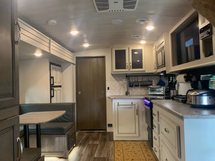 RV rental: Modern and spacious kitchen with white cabinetry, stainless appliances, and a dinette area.. Keystone Cougar Half-Ton 2021
