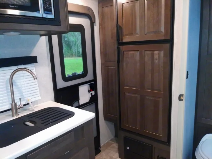 Modern RV rental interior showcasing a compact kitchen with microwave, sink, window, and a large refrigerator.. Forest River Rockwood Mini Lite 2021
