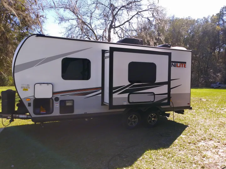 Explore with this modern white & gray rv rental! Travel trailer with slide-out open, parked on green grass near trees.. Forest River Rockwood Mini Lite 2021