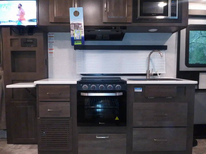 An rv rental's compact kitchen: Magic Chef oven, microwave, sink, and wall-mounted TV. Dark wood cabinetry offers storage.. Forest River Rockwood Mini Lite 2021