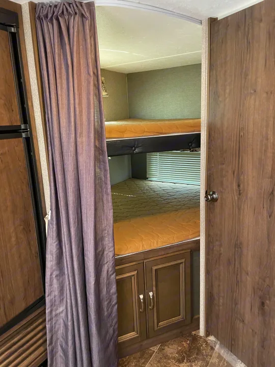 RV rental interior: two bunk beds with tan mattresses, a privacy curtain, storage cabinet, and window blinds.. Keystone Passport 2400BHWE 2018