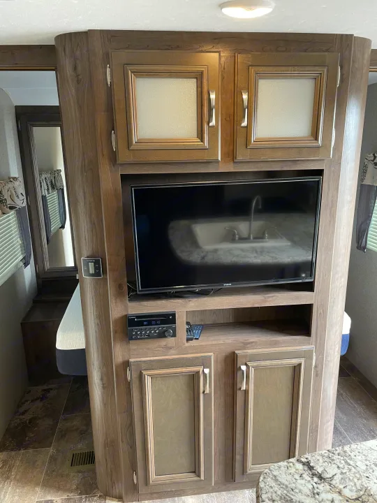 Modern RV rental interior featuring a TV, stereo, ample storage cabinets, and a glimpse of the bedroom area.. Keystone Passport 2400BHWE 2018