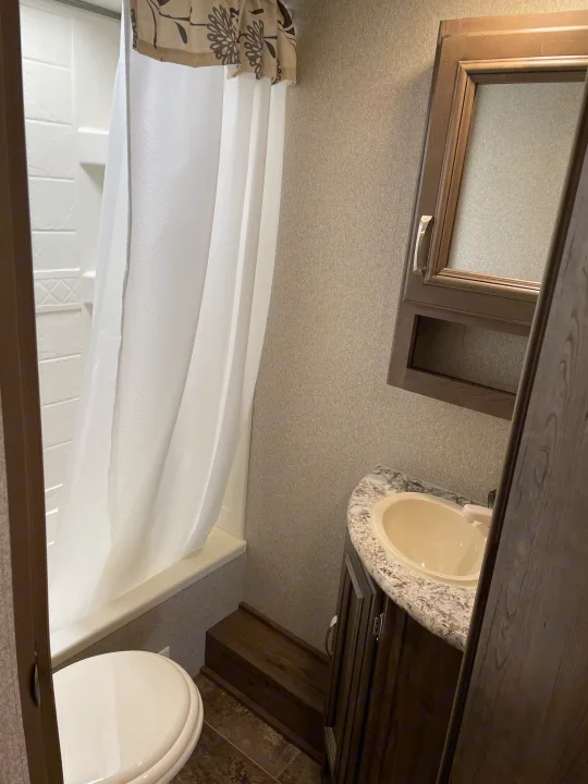 Clean, compact RV rental bathroom featuring a shower, toilet, and vanity with sink and mirror cabinet.. Keystone Passport 2400BHWE 2018