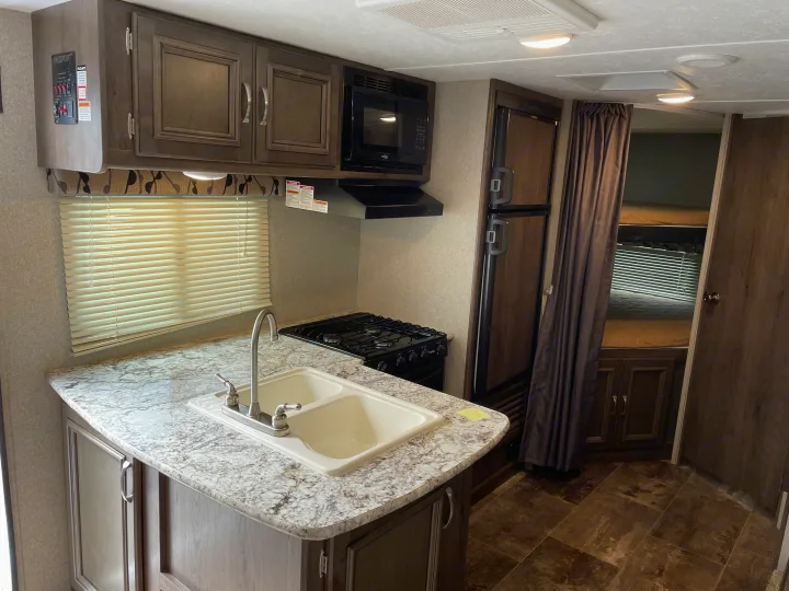 View inside an RV rental showing a full kitchen with sink, stovetop, microwave, refrigerator, and cabinet storage.. Keystone Passport 2400BHWE 2018