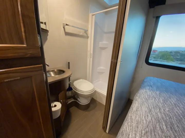 This RV rental showcases a functional compact bathroom with sink, toilet, and shower, plus a sleeping area and window.. Winnebago Vita 2020