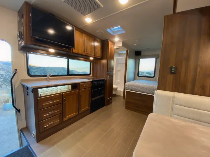 Spacious RV rental interior with kitchen, bedroom, and bathroom areas. Features modern design, tile floor, and mountain views.. Winnebago Vita 2020