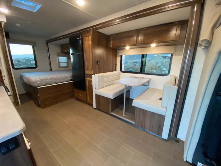 Inside this RV rental, find a cozy dinette, bed, and kitchen area with light wood finishes. Ready for your adventure!. Winnebago Vita 2020
