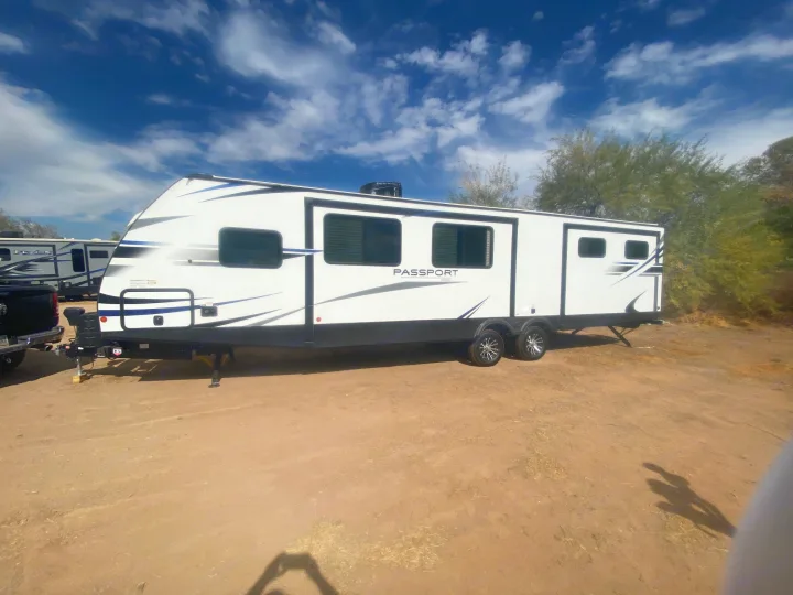 White Passport travel trailer RV rental with blue accents, parked on dirt. Perfect for outdoor escapes!. Keystone RV Passport 2021