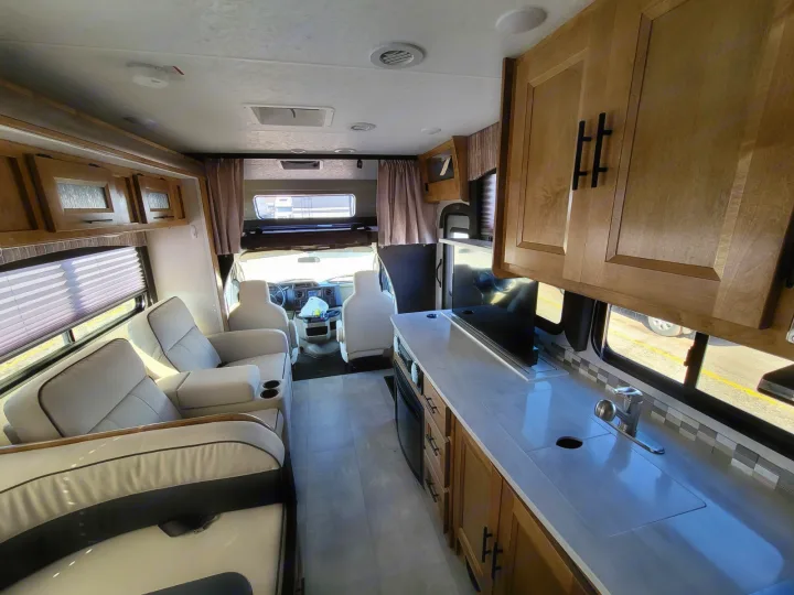 Spacious RV rental interior featuring a cozy living area with recliners, a functional kitchen, and the front cockpit.. Coachmen Leprechaun 2021
