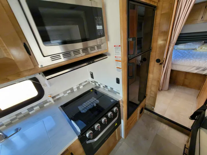 Inside this RV rental: a modern kitchen with a stove, microwave & sink, plus a comfy bedroom with a large bed.. Coachmen Leprechaun 2021
