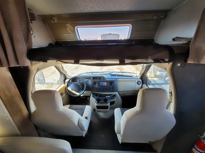 RV rental interior: Front cabin view with dashboard, steering wheel, and comfortable swivel seats.. Coachmen Leprechaun 2021