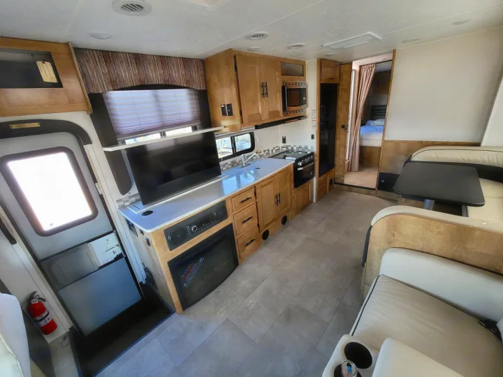 RV rental interior with modern kitchen, TV, fireplace, dinette, and rear bedroom access.. Coachmen Leprechaun 2021