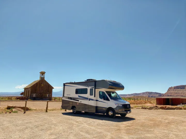 Explore the scenic desert! This Winnebago Porto rv rental is parked by a historic schoolhouse under a clear sky.. Winnebago Porto 2020