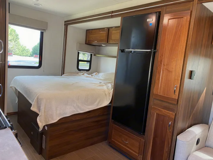 Cozy RV rental interior showcasing a comfortable bed, a black refrigerator, and rich wooden cabinetry for storage.. Winnebago Porto 2020