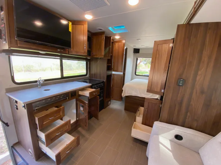 Detailed RV rental interior featuring a modern kitchen with open drawers/cabinets, stove, and a bedroom area visible in the background.. Winnebago Porto 2020