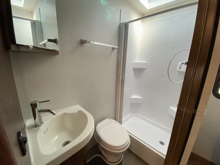 A bright, compact RV rental bathroom with a white sink, modern faucet, toilet, and a stand-up shower with glass door.. Winnebago Porto 2020