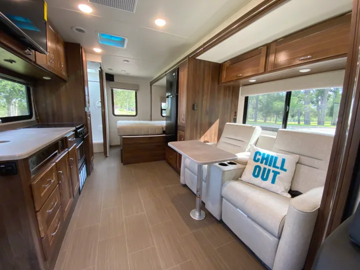Bright, clean RV rental interior features a modern kitchen, comfy recliners with table, and bed area. Your next adventure awaits!. Winnebago Porto 2020