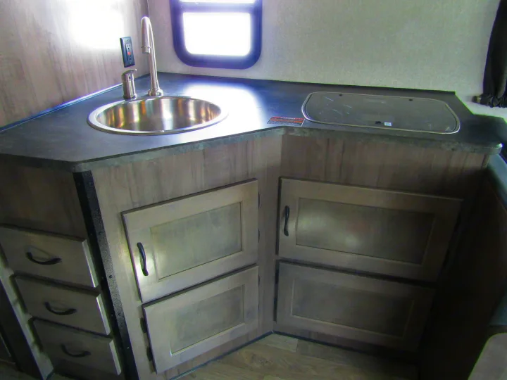Modern RV rental kitchen with a stainless steel sink, covered cooktop, and light wood-tone cabinets.. Winnebago Minnie Winnie 2020