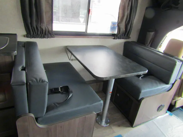 Inside an RV rental: a modern dinette with dark grey cushioned benches, a table, and windows with curtains. Seatbelts are installed.. Winnebago Minnie Winnie 2020