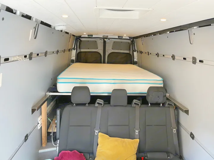 Interior of an RV rental showing a comfy bed and passenger seats in a custom camper van conversion, ready for travel.. Other Sprinter 2019