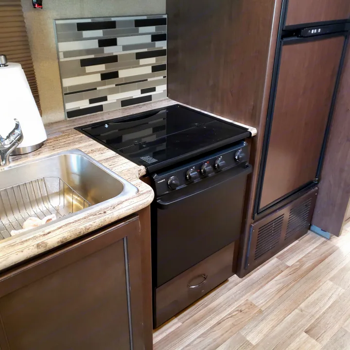 Modern RV rental kitchen with compact sink, stovetop, oven, and fridge, plus a tiled backsplash.. Thor Motor Coach 30.3 2019