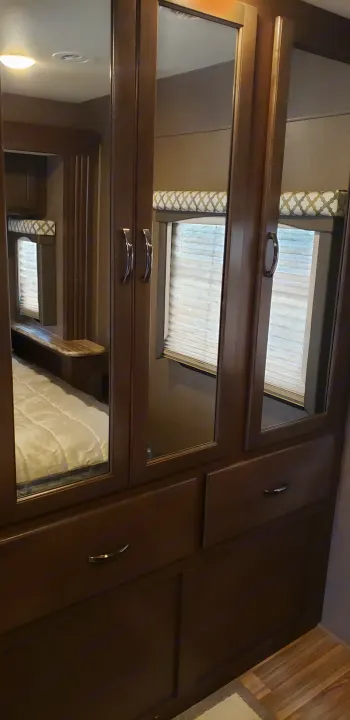 RV rental bedroom: Dark wood wardrobe with mirrored doors and drawers, reflecting the bed and windows.. Thor Motor Coach 30.3 2019