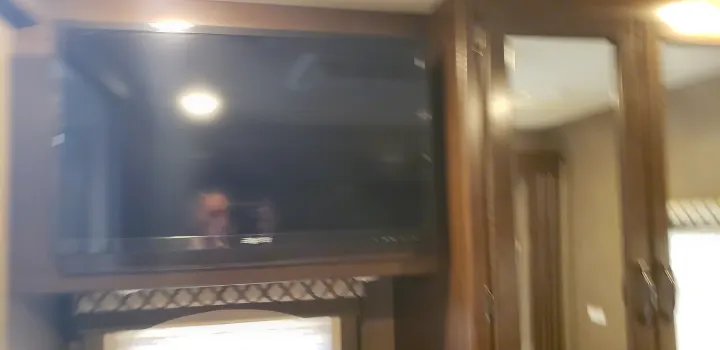 Inside an RV rental: a mounted TV reflects a person and decor, providing entertainment in a compact living space.. Thor Motor Coach 30.3 2019