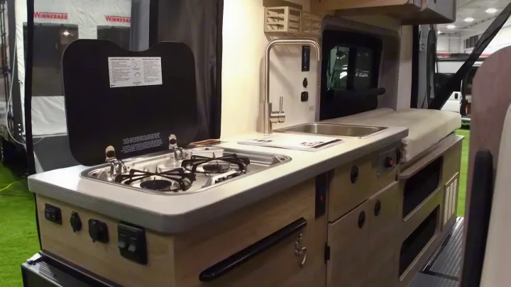 Inside an RV rental camper van: a sleek kitchen area with a stainless steel sink, two-burner stove, and integrated counter space.. Winnebago Solis 2021