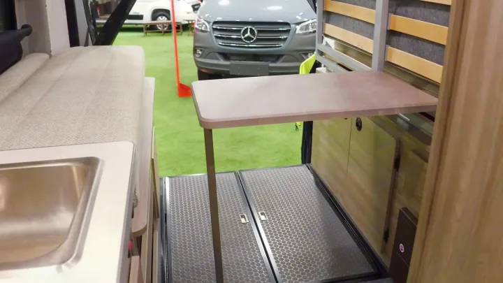 RV rental interior: A compact kitchen sink, pull-out table, bed area, and underfloor storage in a modern camper van.. Winnebago Solis 2021