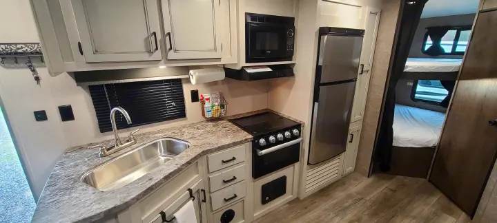 Cozy rv rental interior: full kitchen with sink, stove, microwave, fridge, and bunk beds visible.. Open Range 26BHS 2021