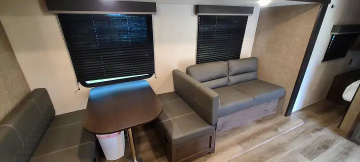 RV rental interior: cozy dinette area with gray bench seating, dark table, and two windows with blinds. Light walls and laminate floor.. Open Range 26BHS 2021