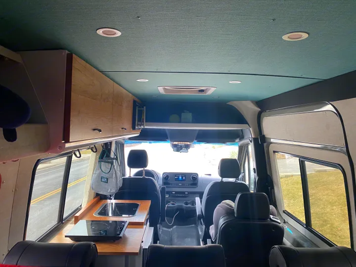 Spacious rv rental interior, featuring the driver's cabin, kitchenette with sink and cooktop, overhead storage, and seating.. Mercedes-Benz Sprinter 2020
