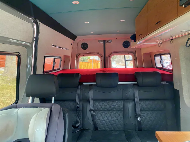 View of an RV rental interior: three quilted seats, raised red bed, teal ceiling, and custom cabinets. Ready for travel.. Mercedes-Benz Sprinter 2020