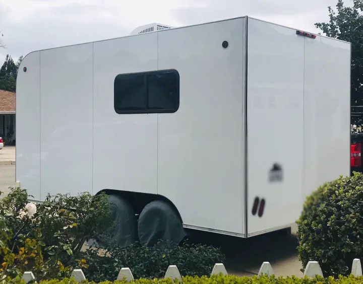This white RV rental trailer, featuring a side window and covered wheels, is ready for your next adventure.. Custom Camper Trailer 2020