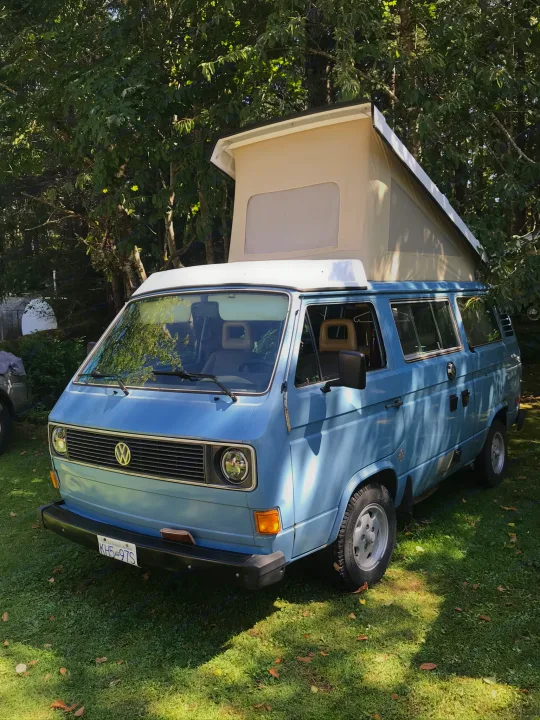This light blue VW Vanagon pop-top camper, parked on grass amidst trees, is perfect for your next rv rental adventure.. Volkswagen Westfalia 1981