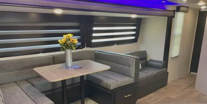 Spacious RV rental dinette area with gray bench seating, light table, and modern blinds. Features comfortable lounge seating to the right.. Forest River Grey Wolf 29te 2021