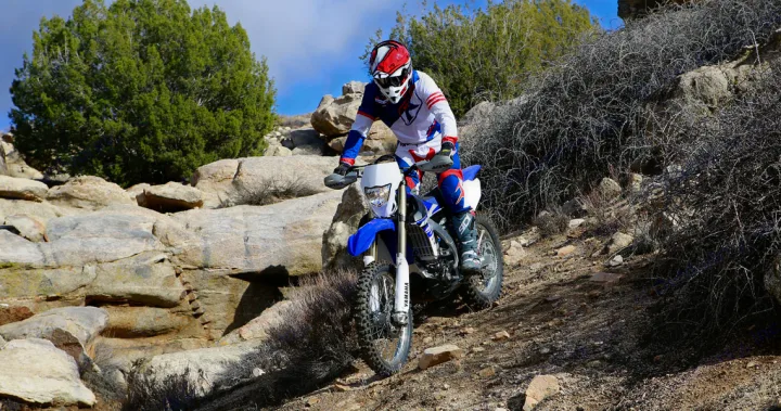 A motorcyclist on a blue dirt bike descends rocky off-road terrain. Ideal adventure after an RV rental, exploring rugged landscapes.. Yamaha WR250F 2015