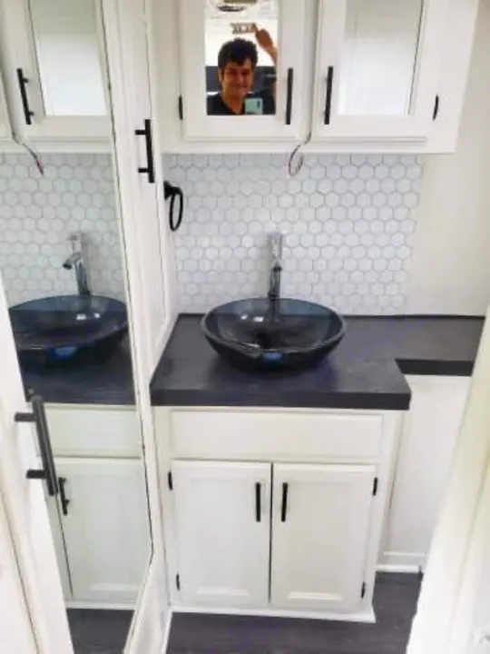 Explore our RV rental: modern bathroom with black vessel sink, white cabinets & hexagonal tile. Person reflected in mirror.. Safari Trek 2610 1994