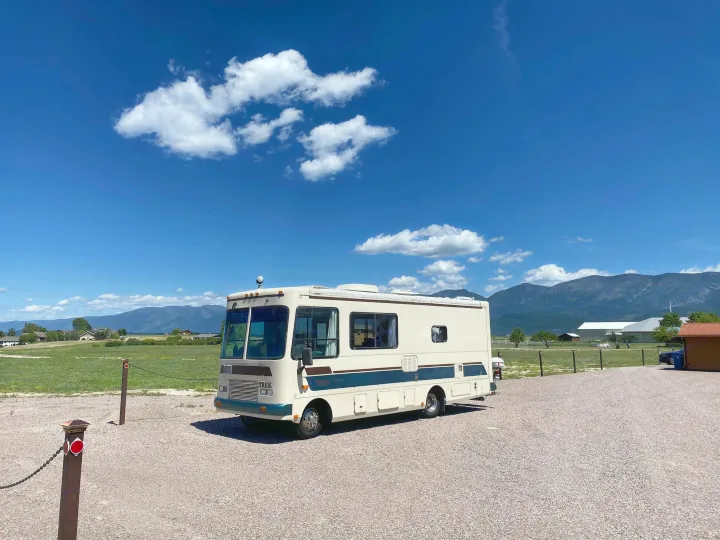 This cream & blue RV rental is parked on a gravel lot, ready for adventure with mountains & blue sky.. Safari Trek 2610 1994