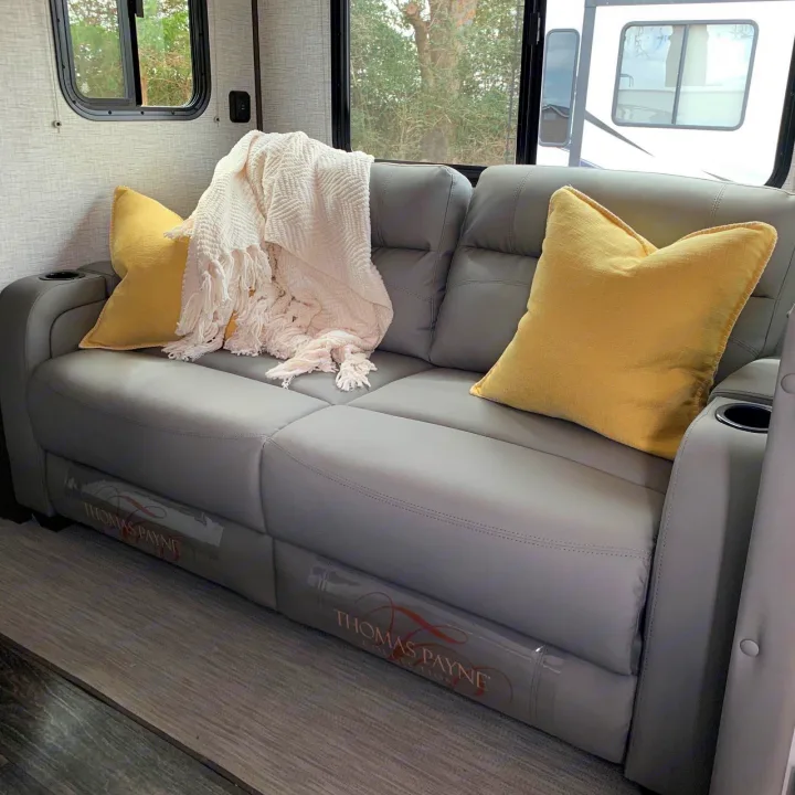 Relax on this comfortable gray Thomas Payne recliner sofa with yellow pillows and white blanket in your rv rental.. Keystone RV Bullet Ultra Lite 2021